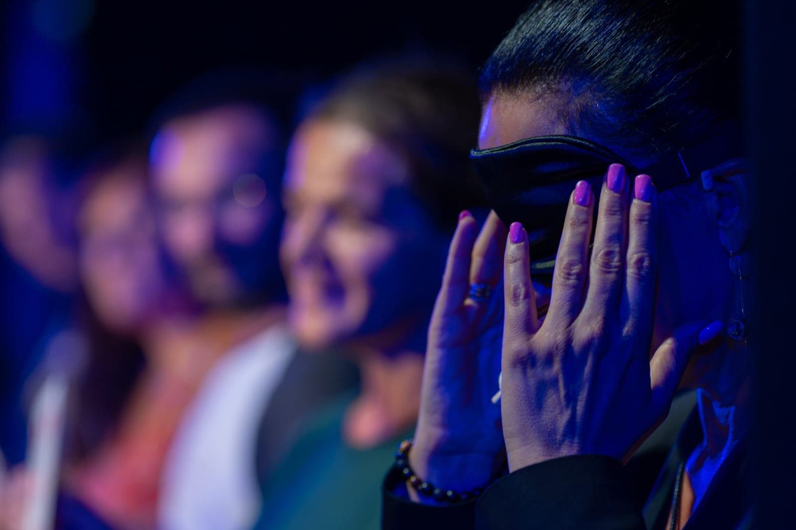 Karine, les yeux couverts d’un bandeau, les mains sur les tempes, devant des spectateurs flous