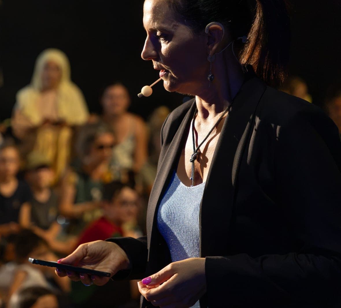 Karine de profil face à son public en plein air, dans la lumière chaude de fin de journée