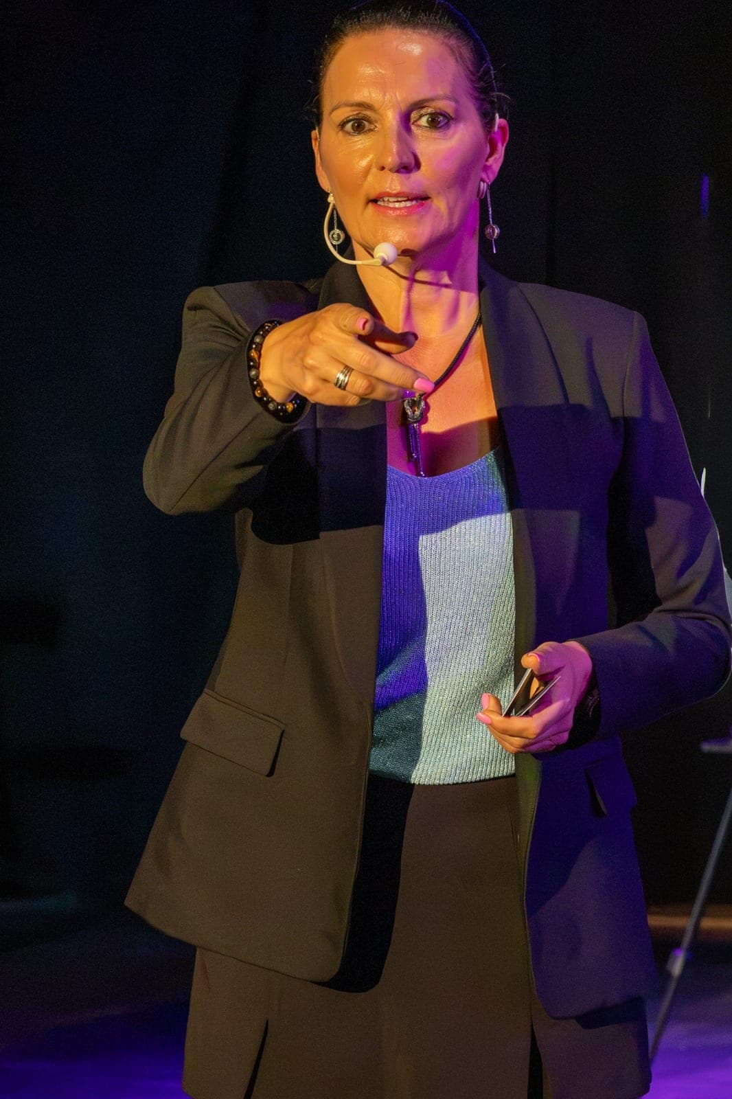 Portrait de Karine désignant le public du doigt, dans une lumière violette